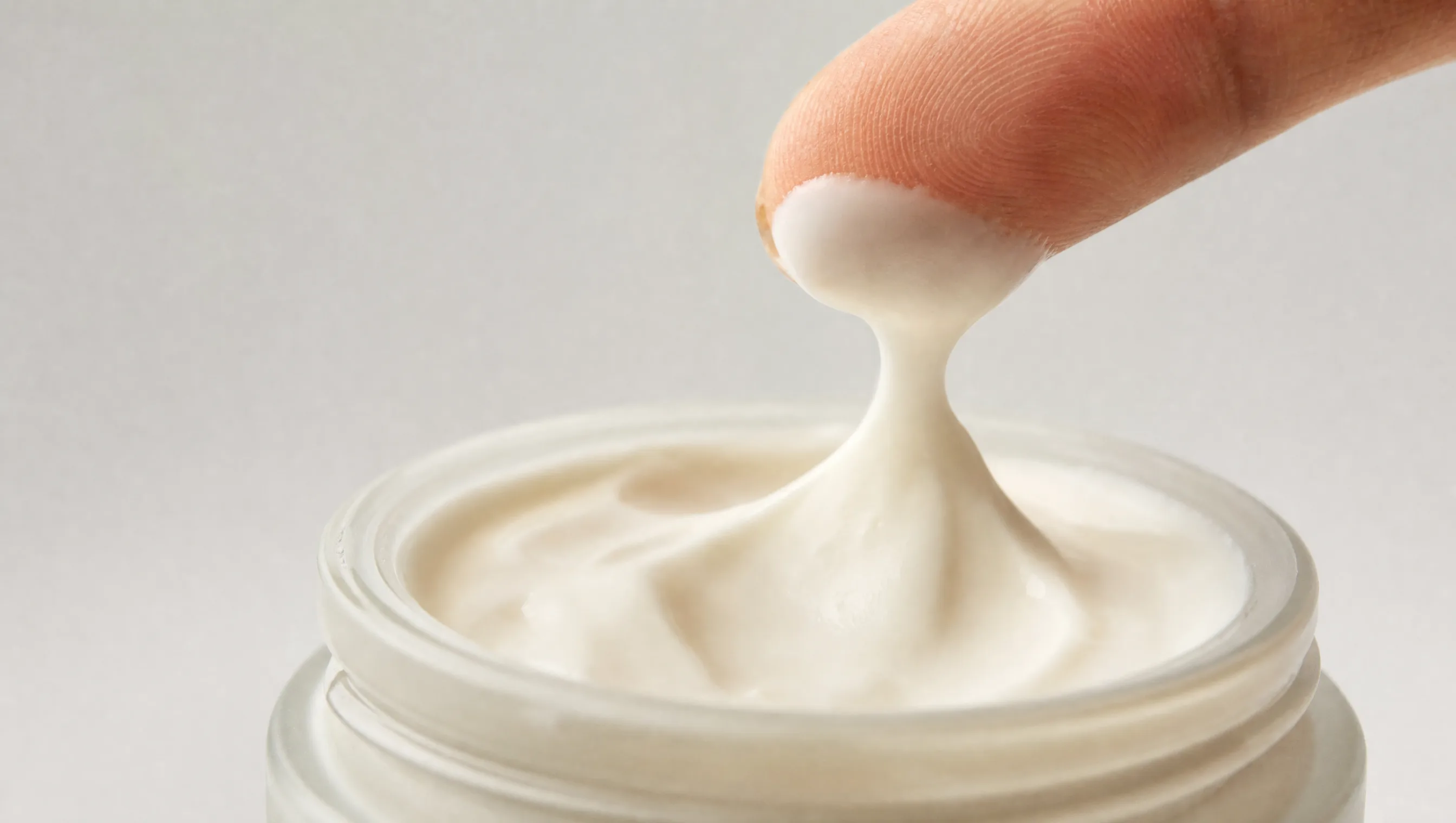Fingertip lifting a small amount of thick barrier-repair moisturiser cream